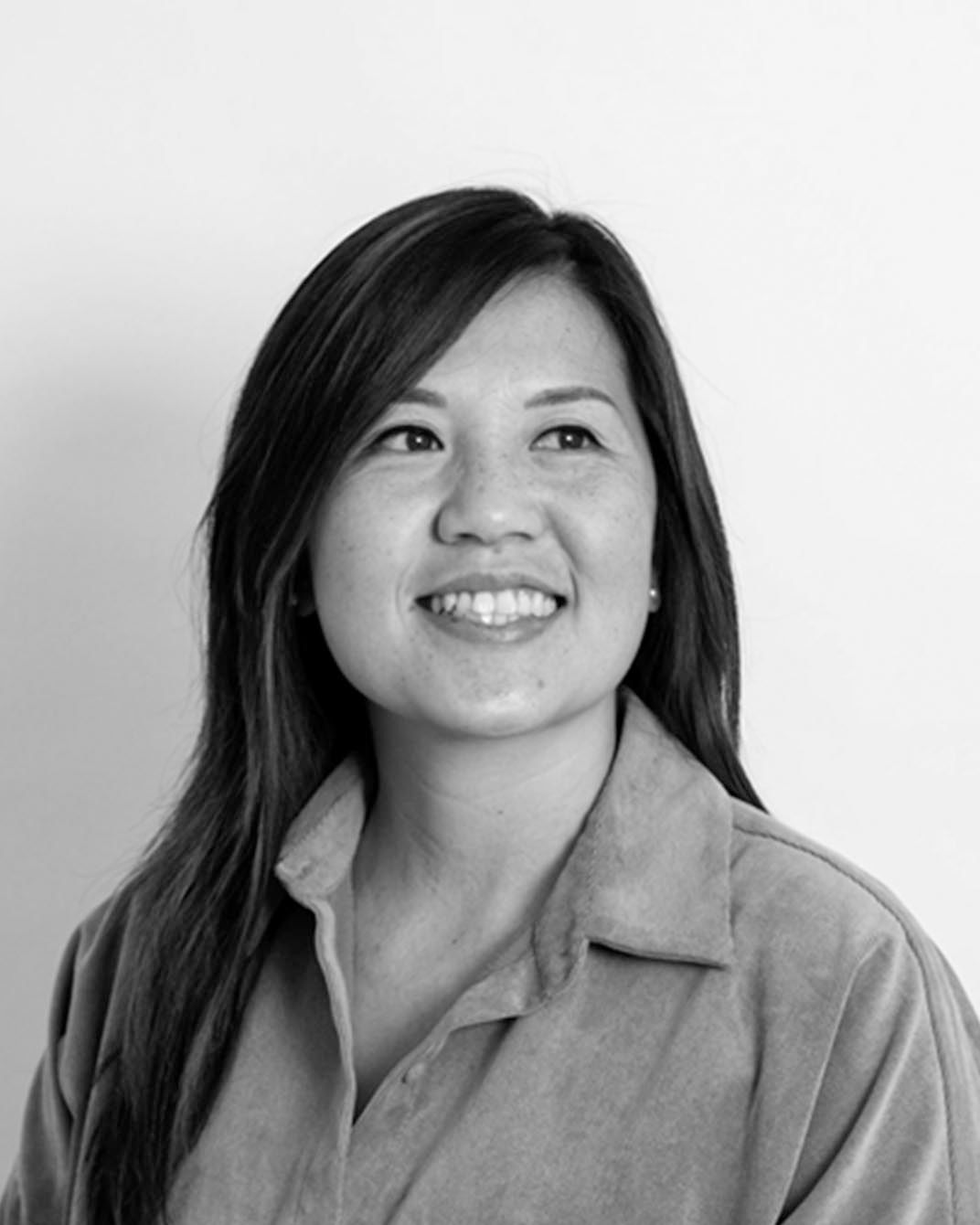 Smiling woman in a light shirt, looking off-camera against a plain background