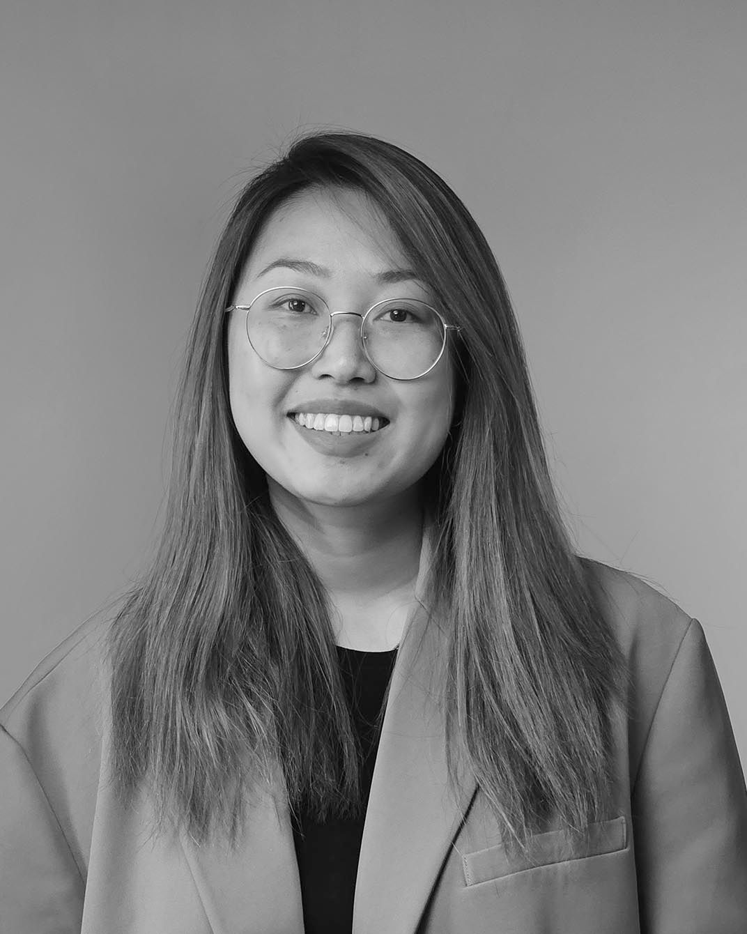 Portrait of a smiling person with glasses and long hair against a plain gray background