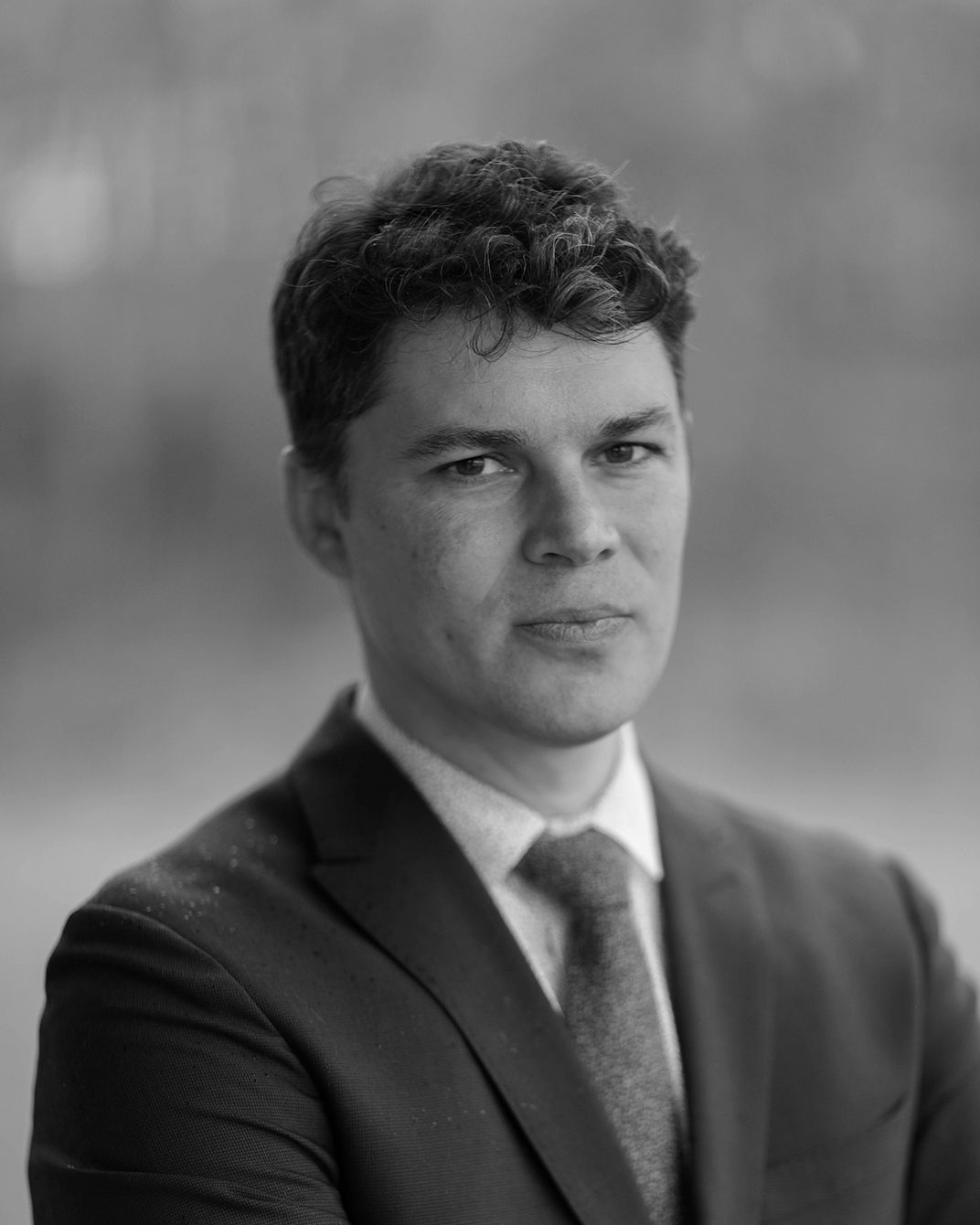 Portrait of a man in a suit and tie against a blurred background.