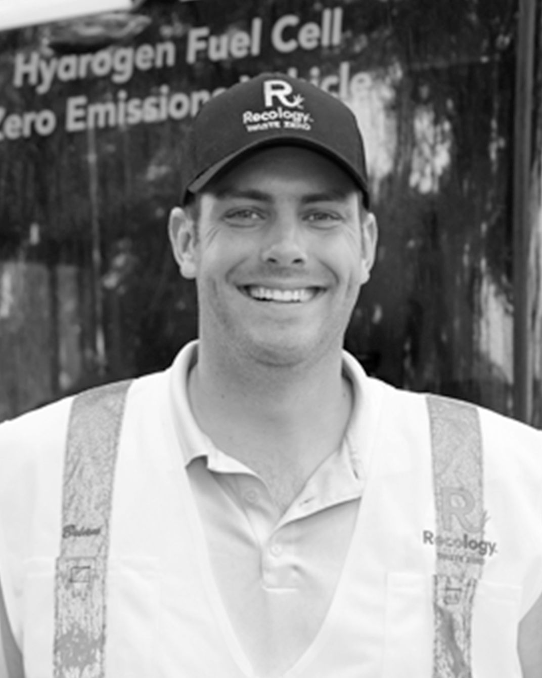 Smiling man in a cap and safety vest standing before a hydrogen fuel cell vehicle display