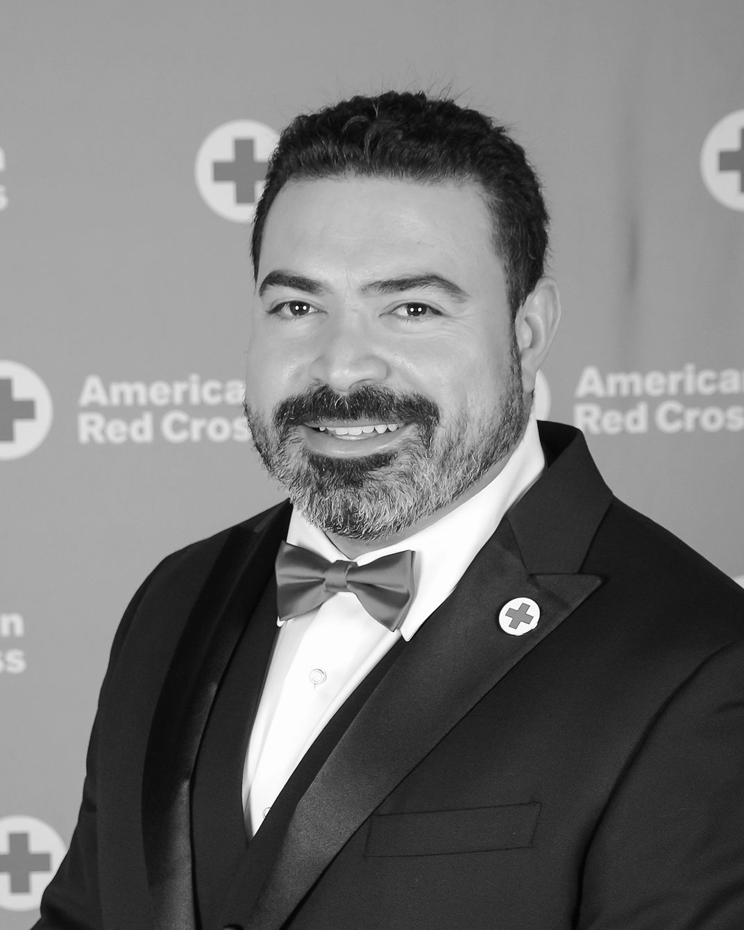 Man in a tuxedo smiling at an American Red Cross event backdrop