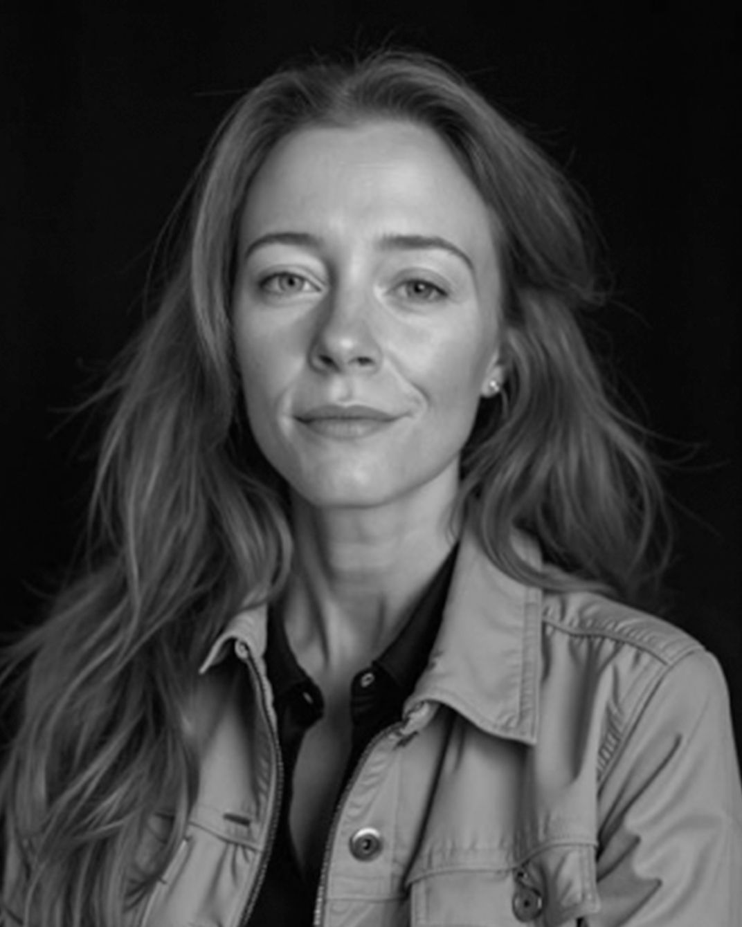 Black-and-white portrait of a woman with long hair wearing a light jacket against a dark background