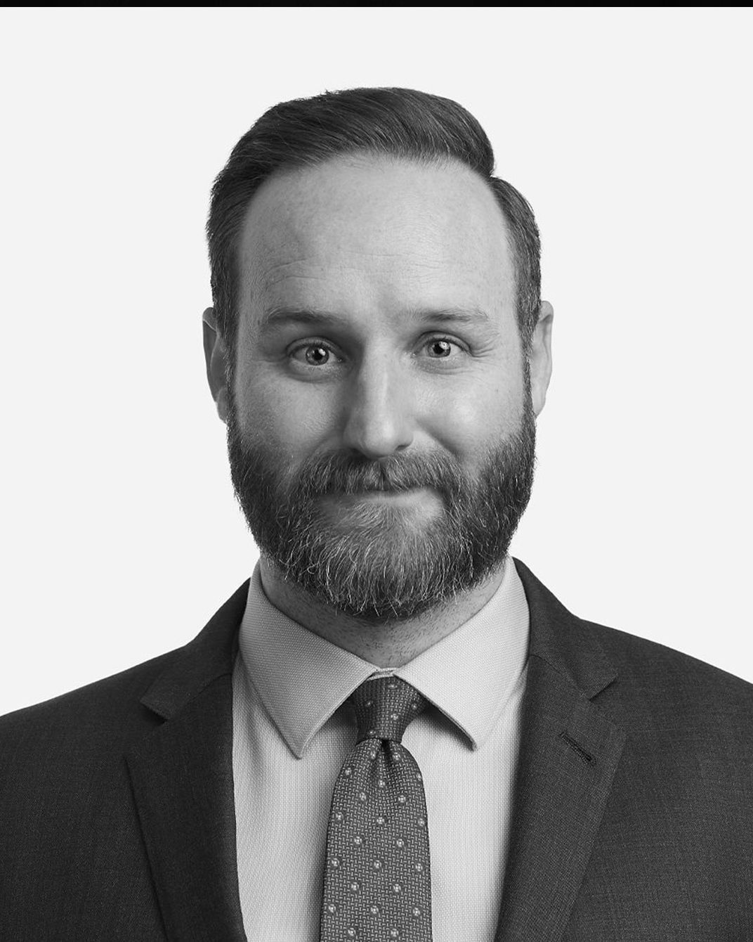 Black-and-white portrait of a smiling man in a suit, shirt, and tie against a plain background