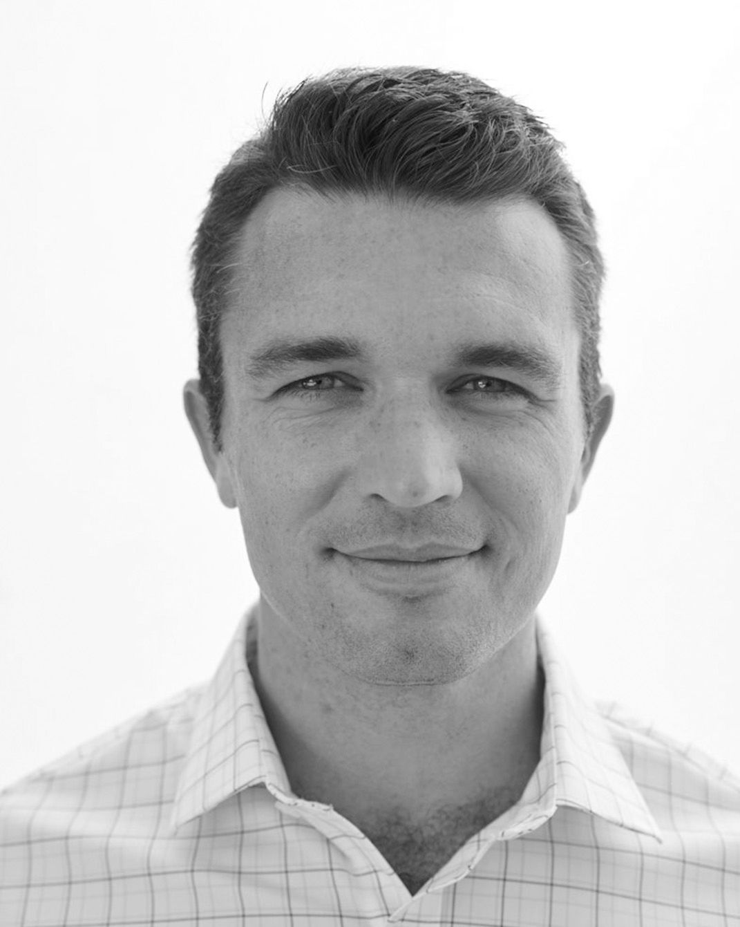 Black-and-white headshot of a smiling man in a collared shirt against a plain background