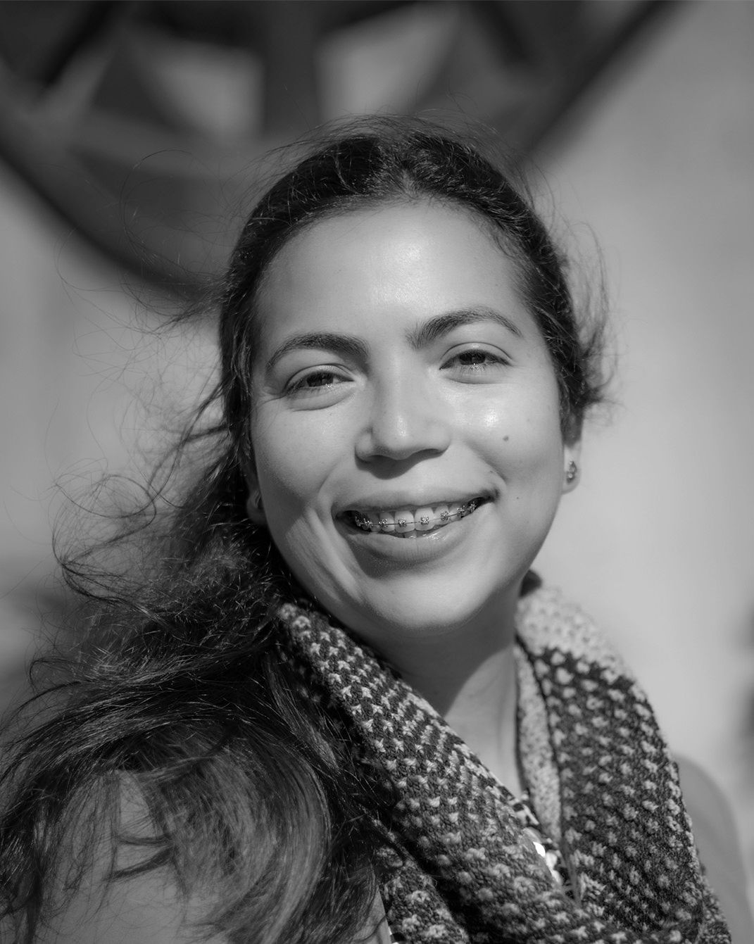 Smiling person outdoors, wearing a patterned scarf, in black-and-white portrait