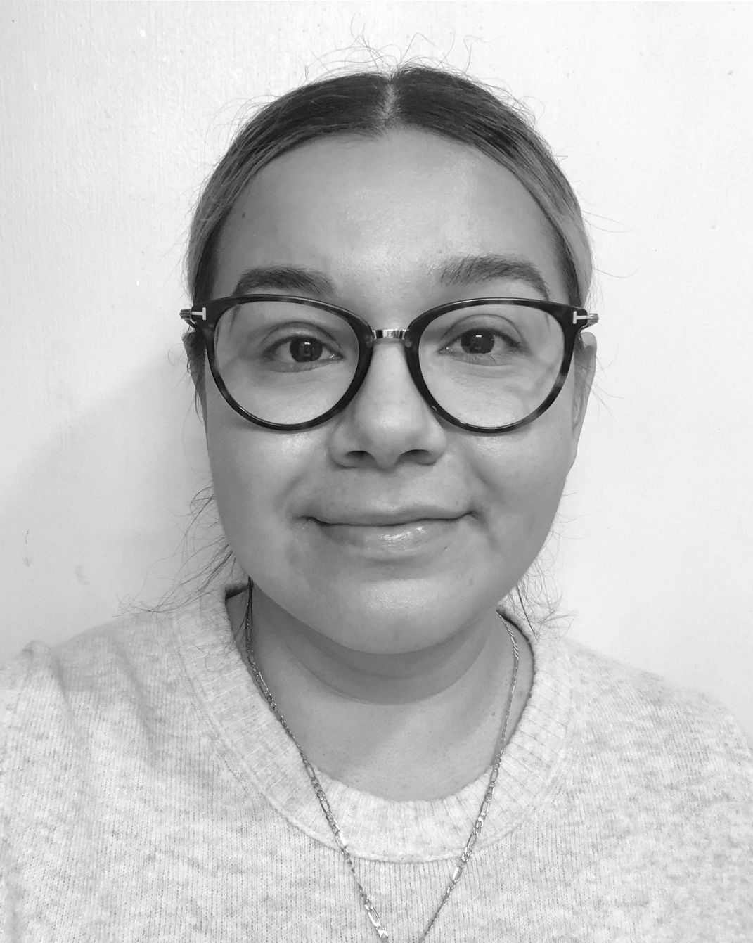 Person wearing round glasses and a light sweater, looking at the camera with a slight smile.
