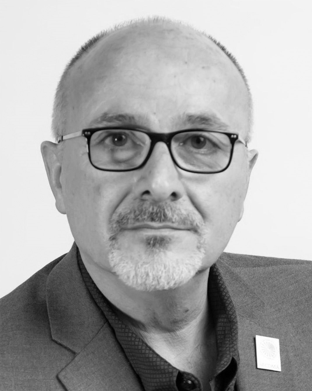 Portrait of a bald man with glasses in a suit, looking at the camera.