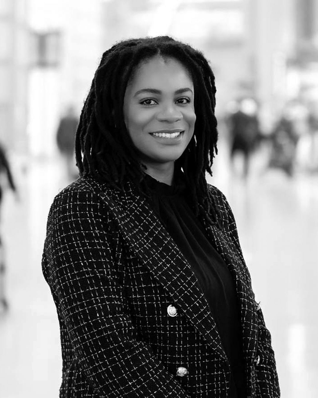 Smiling person in a dark tweed jacket standing in a bright hallway