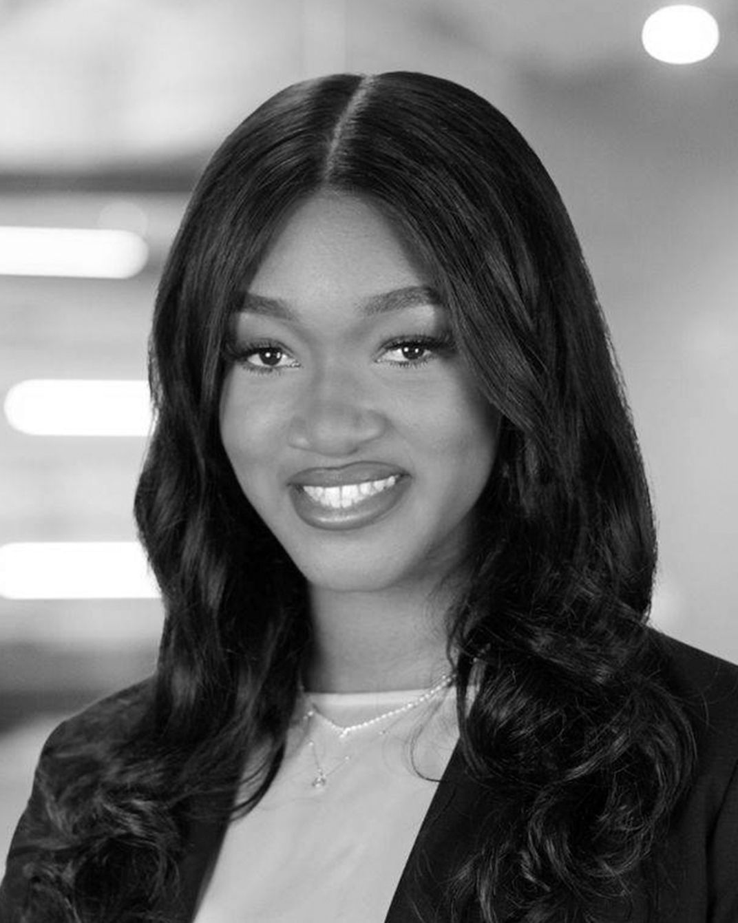 Portrait of a smiling person in a dark blazer against a blurred indoor background