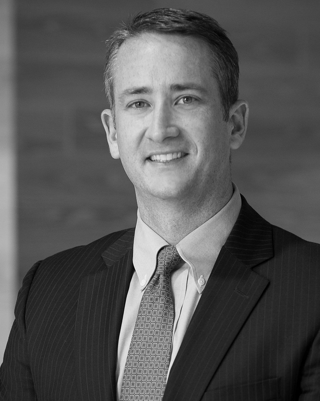 Portrait of a man in a suit and tie, smiling against a plain background