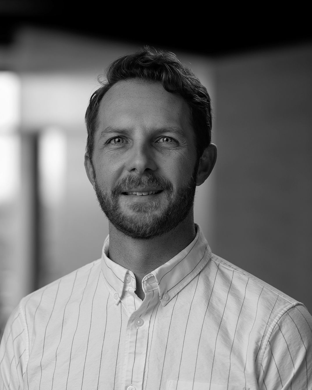 Black-and-white portrait of a man in a light button-up shirt, looking at the camera with a slight smile.