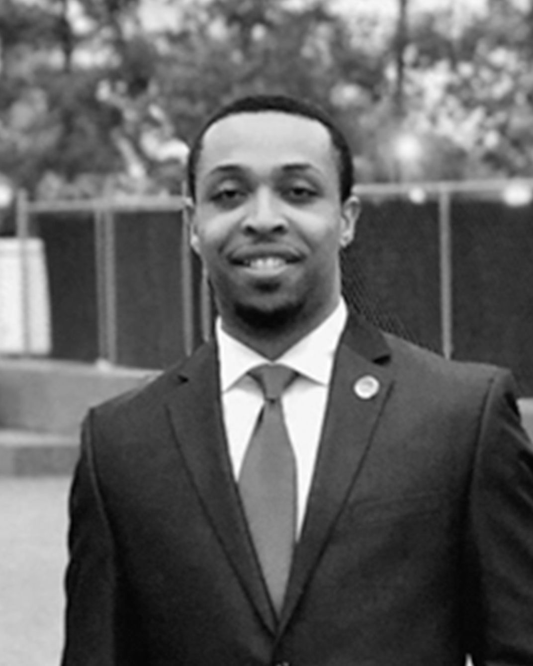 Man in a dark suit and red tie standing outdoors, smiling in a black-and-white portrait.