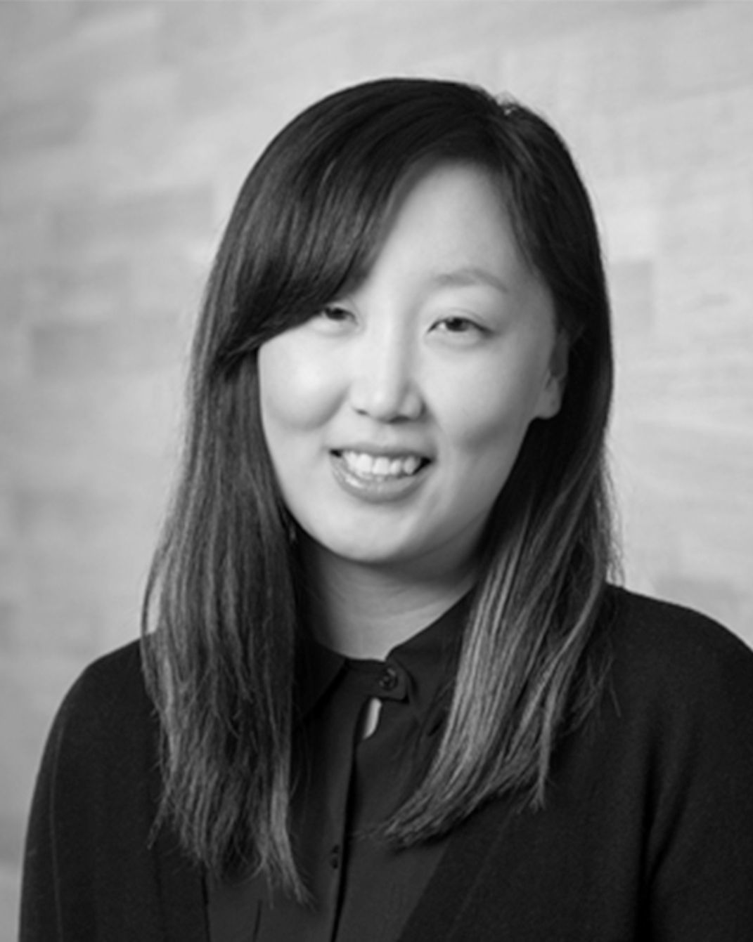 Portrait of a smiling woman with long dark hair against a softly blurred gray background
