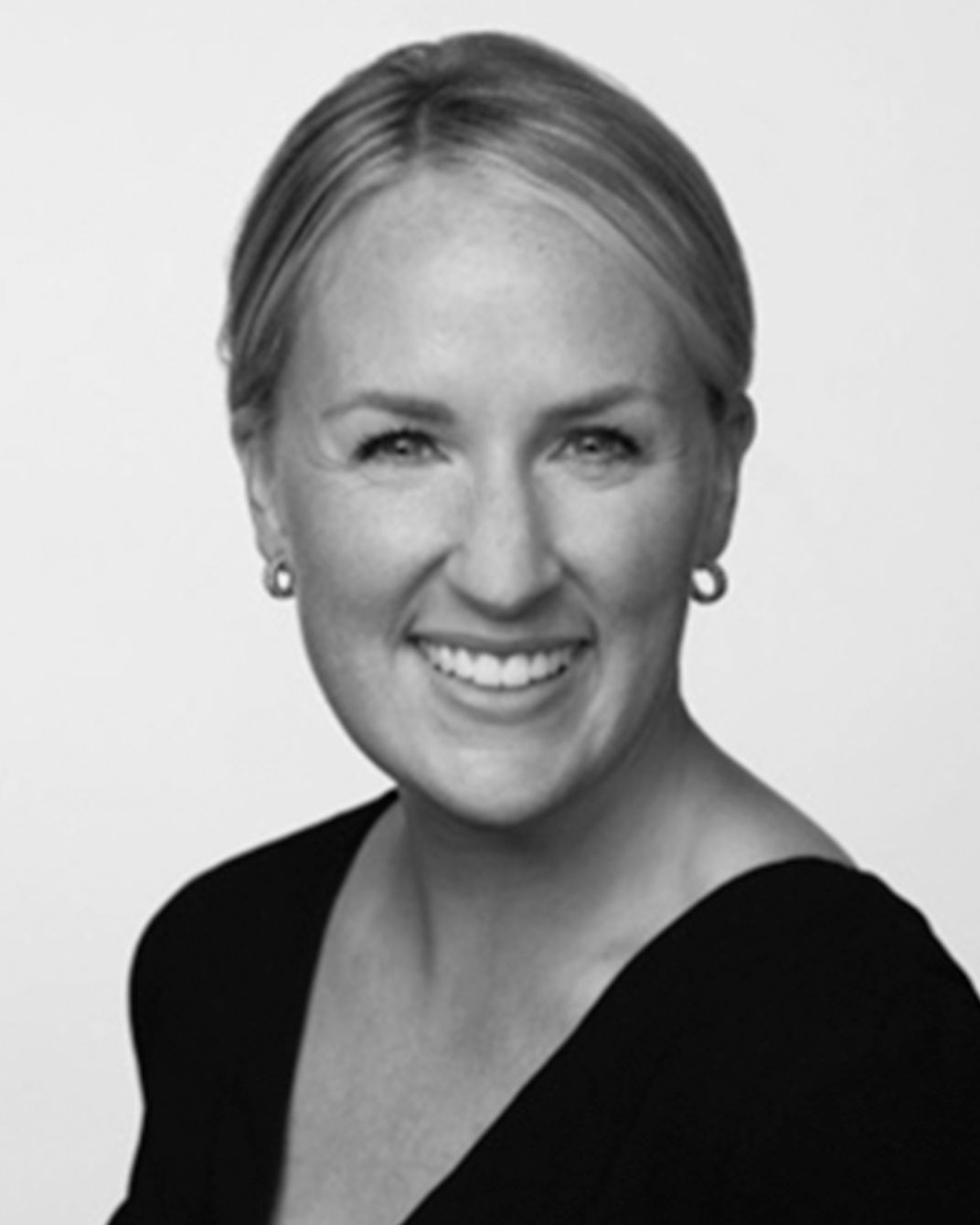 Black-and-white portrait of a smiling person in a dark top, against a plain background