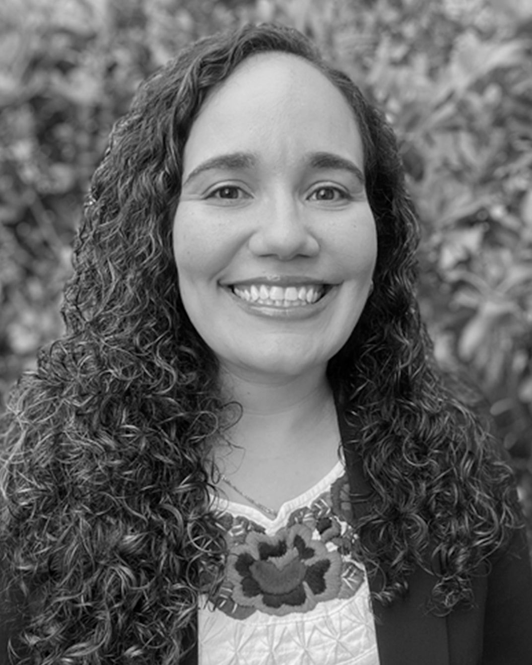 Smiling person with curly hair in a black-and-white portrait outdoors