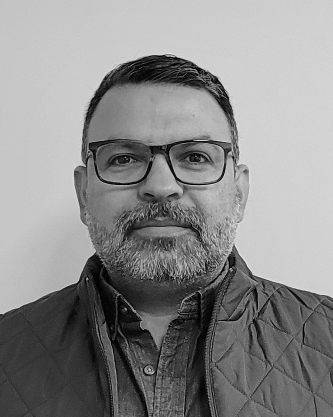 Portrait of a man wearing glasses and a quilted jacket, looking at the camera