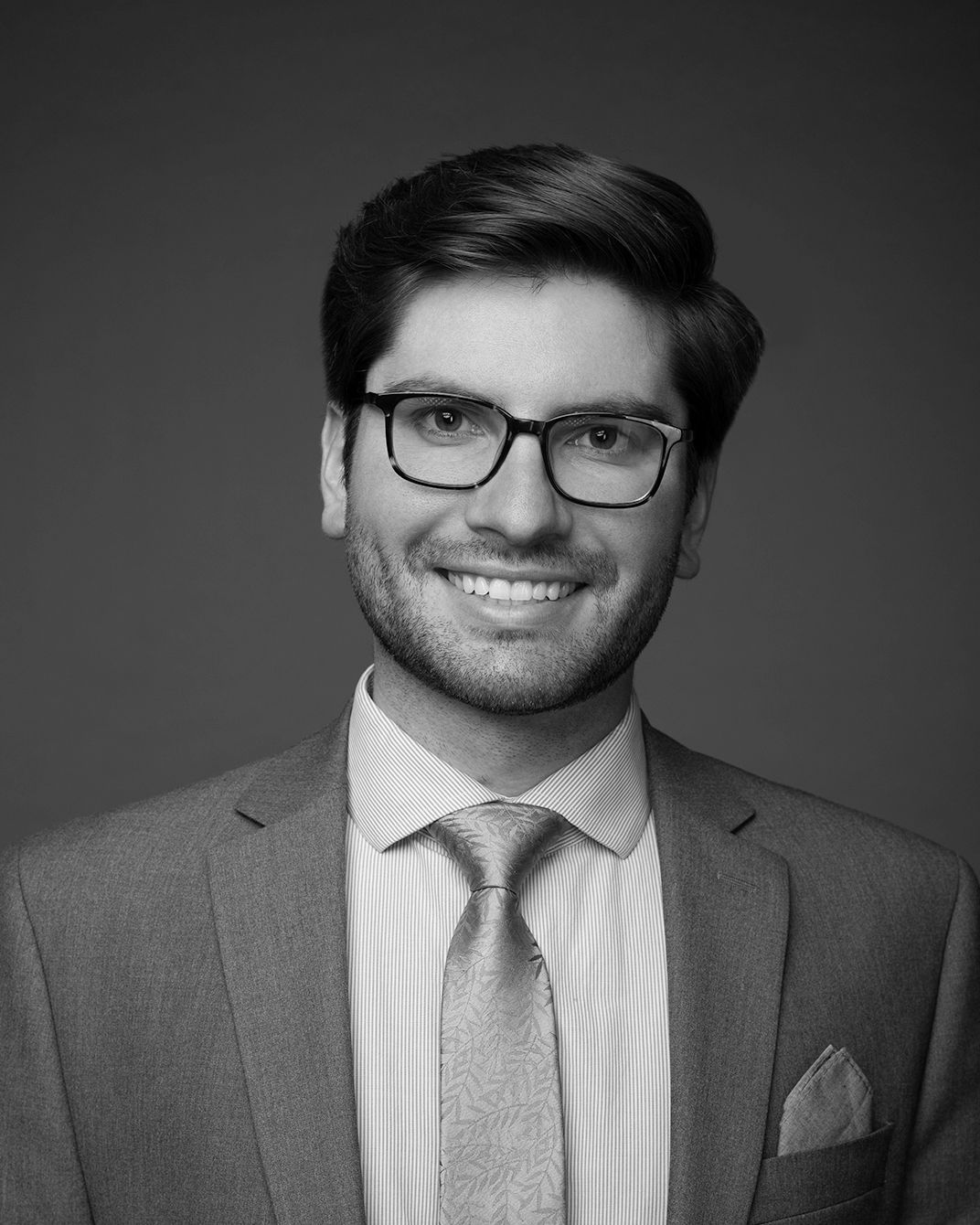 Smiling person in glasses and suit against a dark gray studio background
