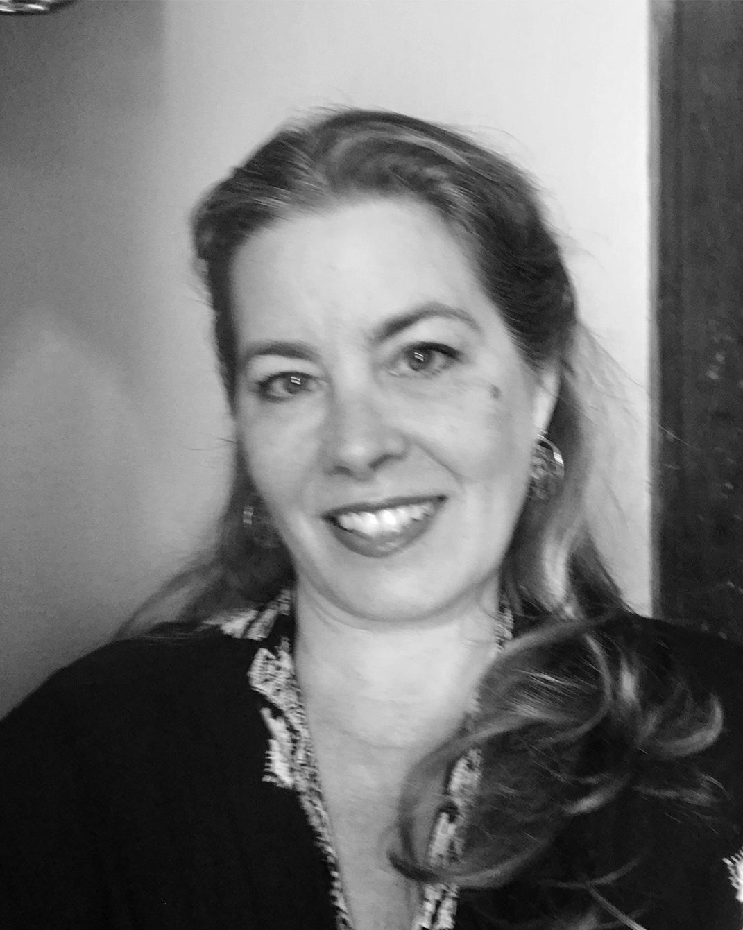 Black-and-white portrait of a smiling woman with long hair, wearing a dark top and earrings.