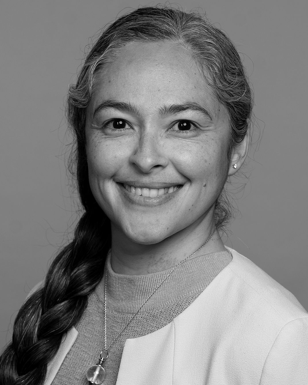 Smiling woman with a braid wearing a light sweater and cardigan against a plain background