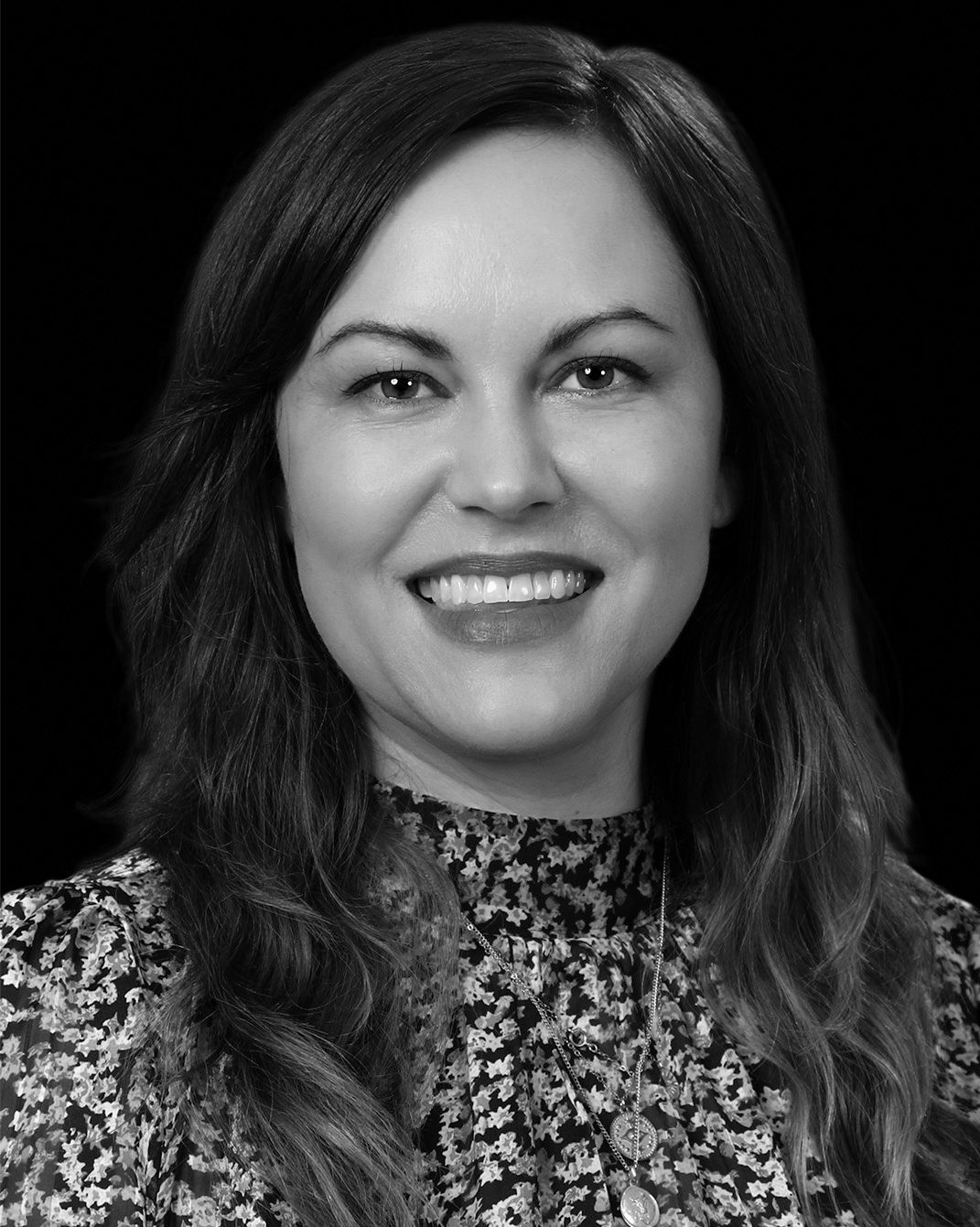 Black-and-white portrait of a smiling person with shoulder-length dark hair in a patterned blouse
