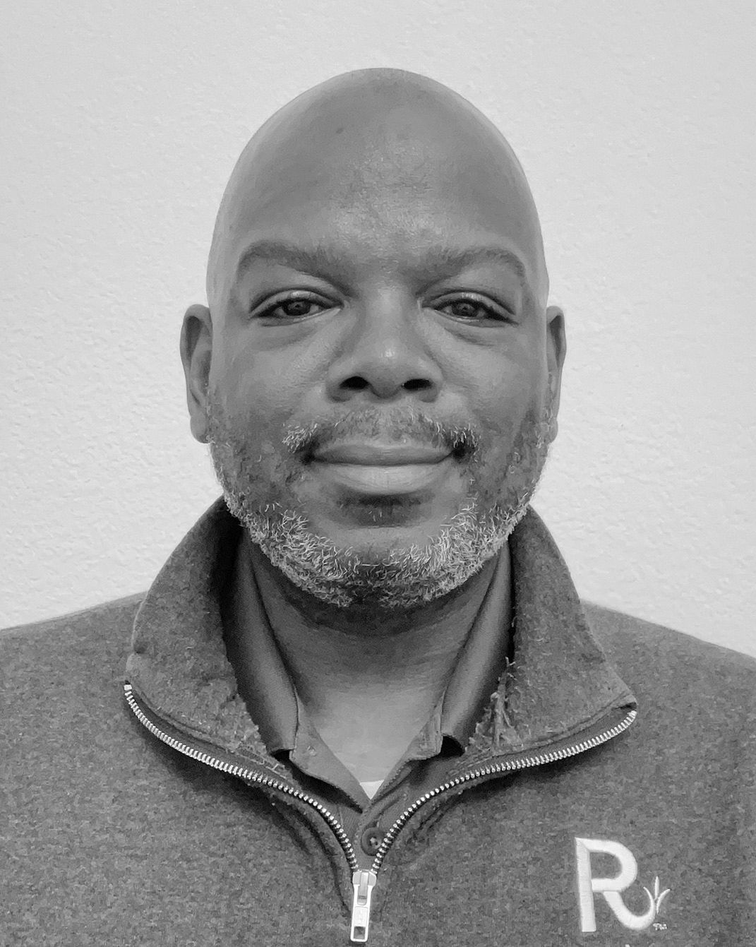 Portrait of a smiling bald man in a gray zip-up sweater against a plain background