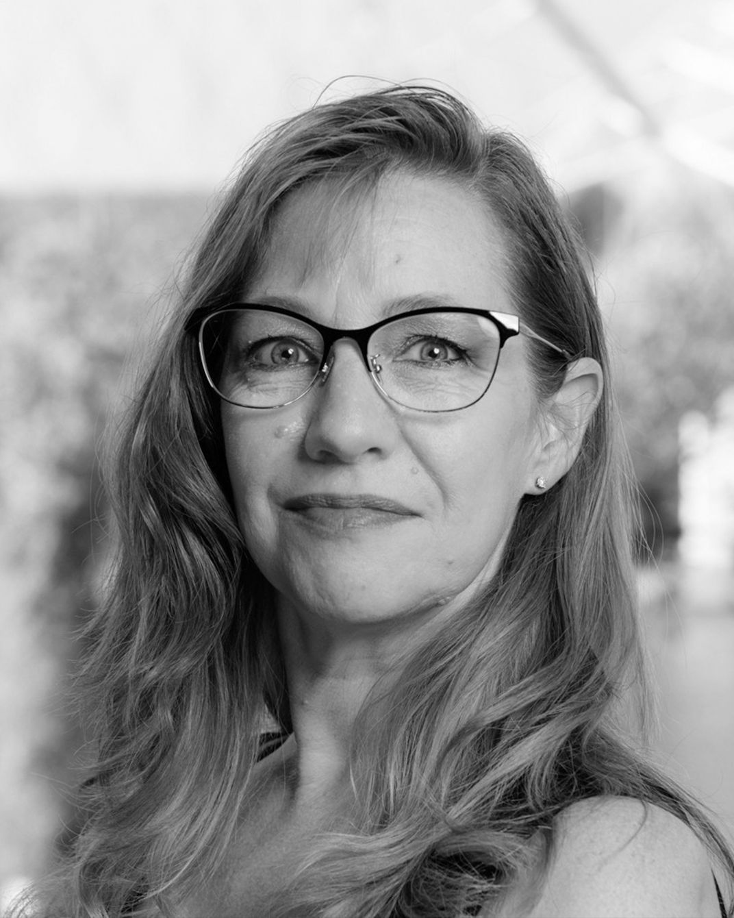 Black-and-white portrait of a woman with glasses and long hair, looking at the camera
