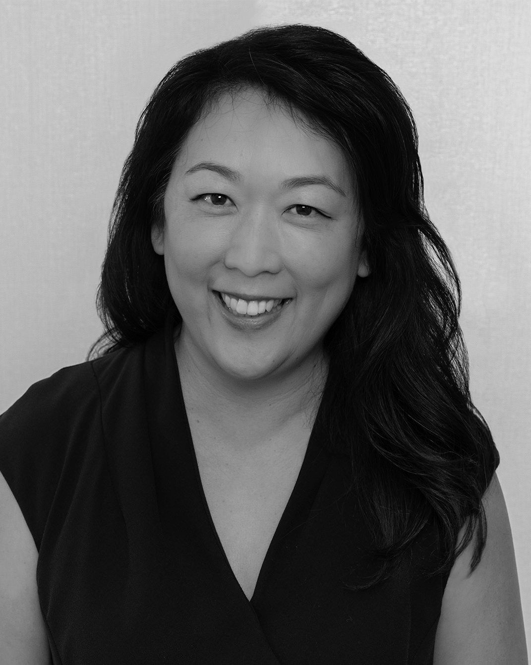 Smiling woman with long dark hair wearing a black top against a light background