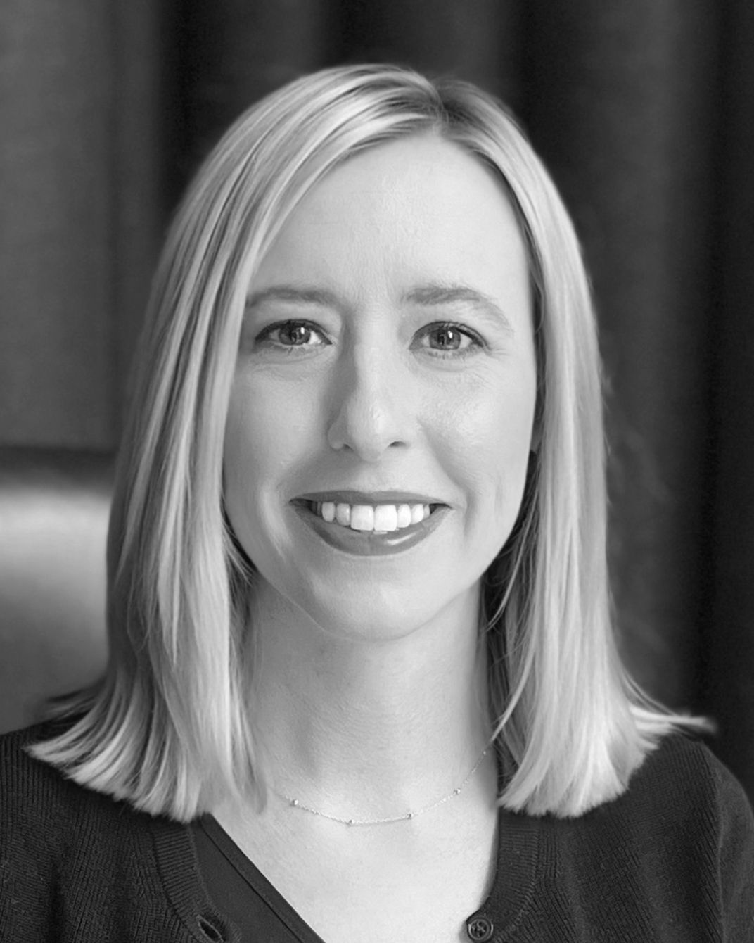 Portrait of a smiling woman with shoulder-length blonde hair against a dark background
