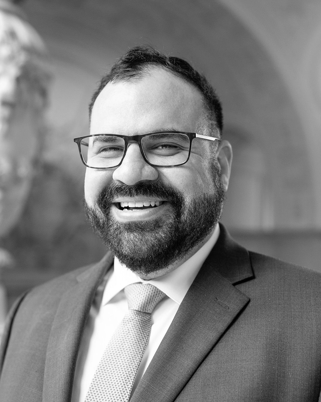 Smiling man in glasses and suit jacket, posing for a portrait indoors.