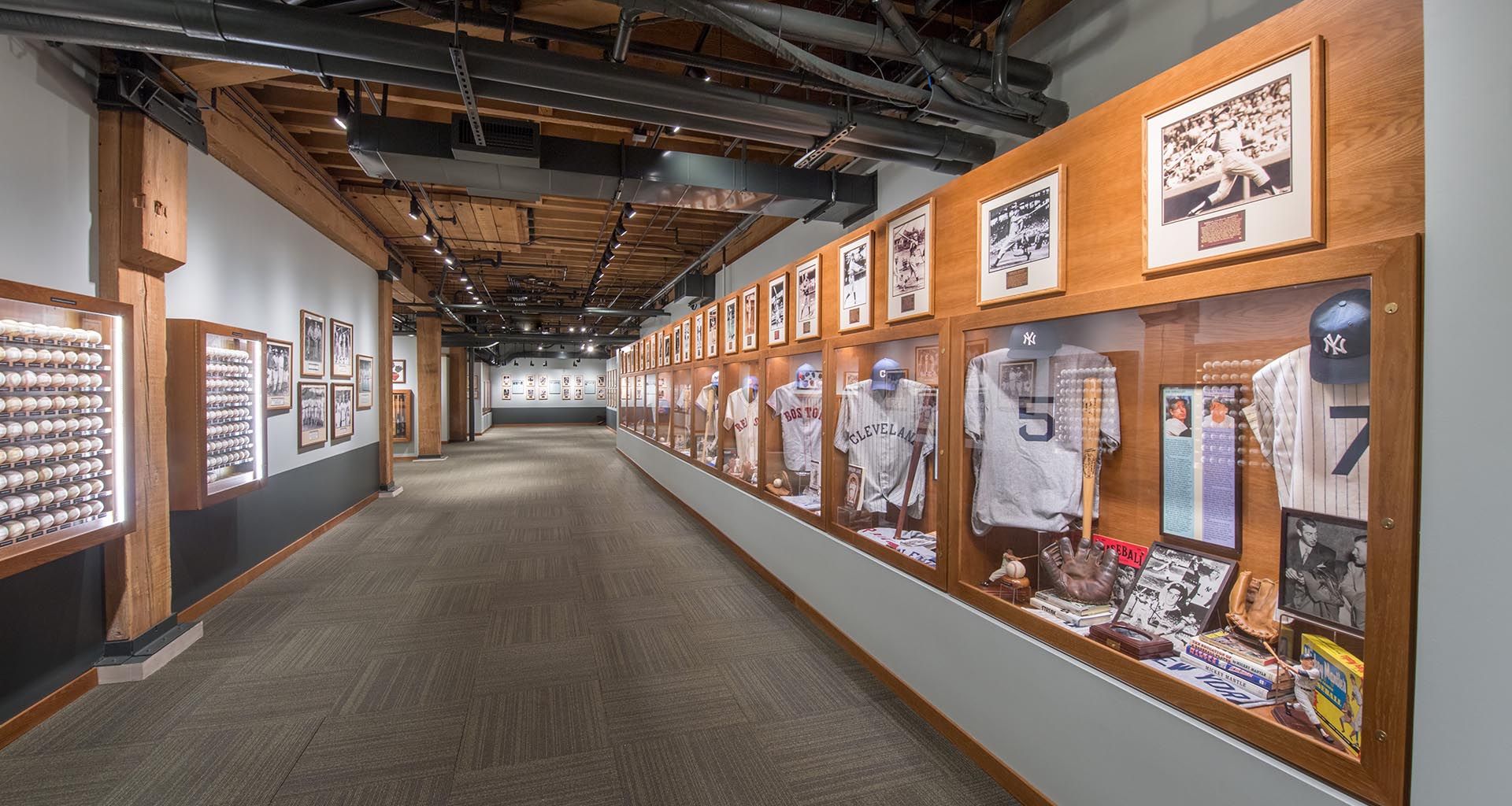 Museum hallway with sports displays, framed photos, and jerseys along wood-paneled walls