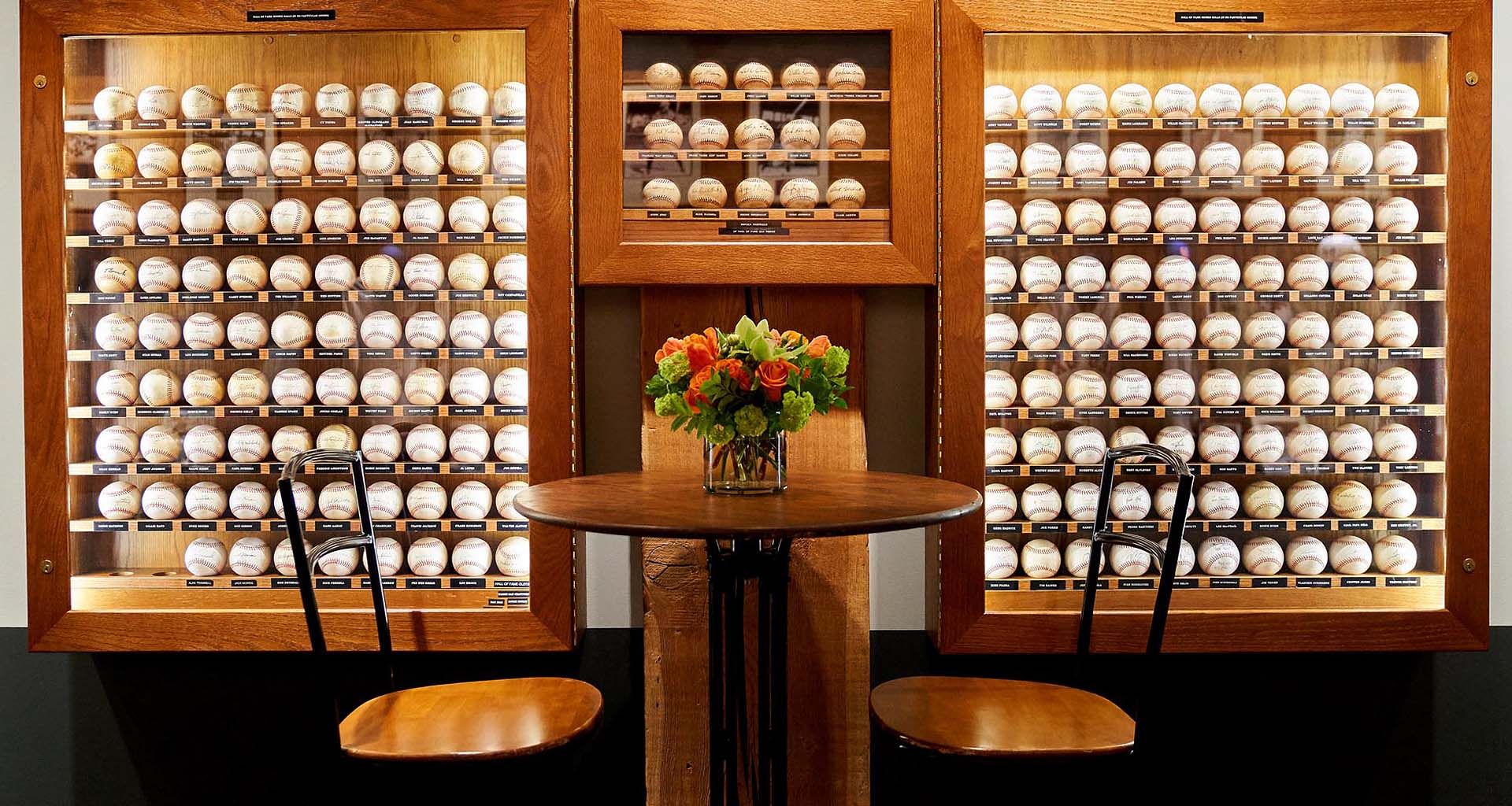 Wood-paneled wall of white ceramic cups with a small flower arrangement on a table and two chairs in front
