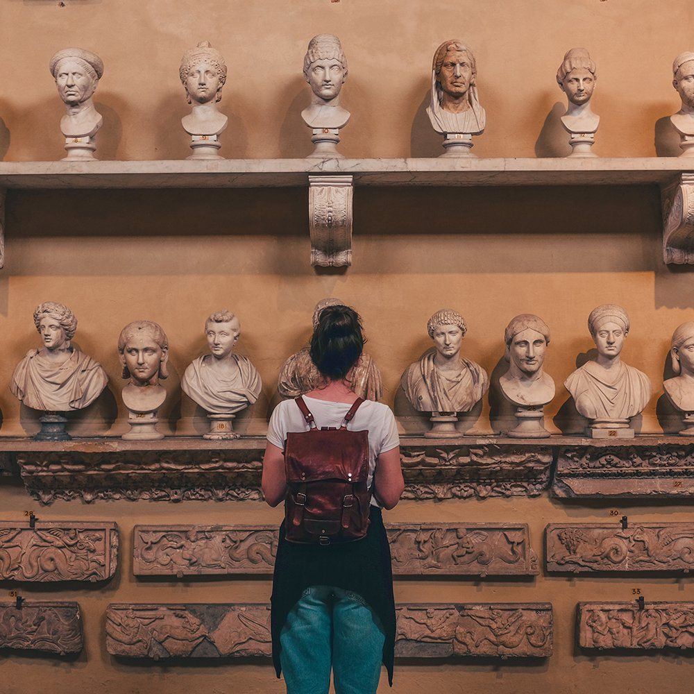 Visitor viewing a wall of classical busts in a museum exhibit