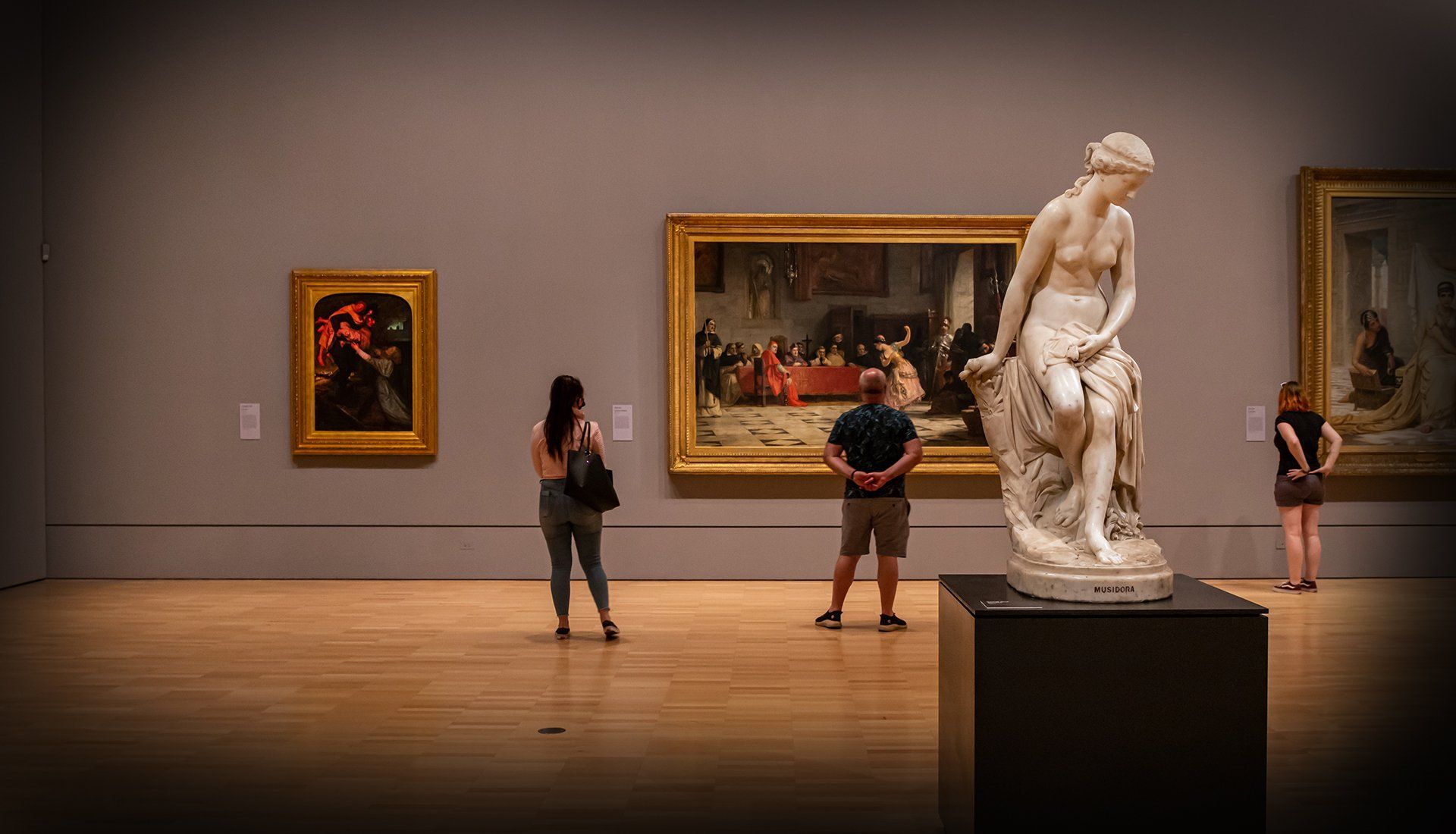 Visitors viewing classical sculptures and paintings in a museum gallery