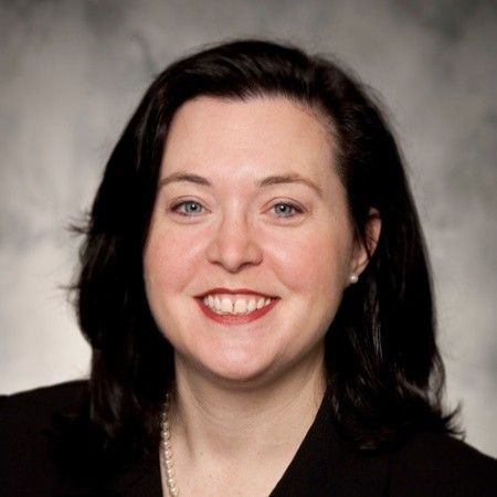 Head-and-shoulders portrait of a smiling woman with dark hair against a gray studio background