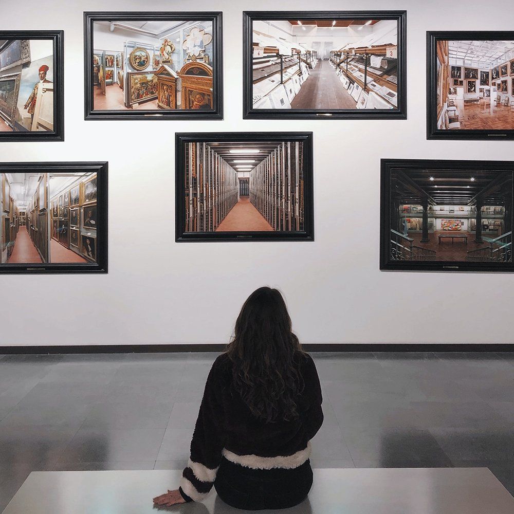 Person seated on a bench viewing framed photos in a gallery wall.