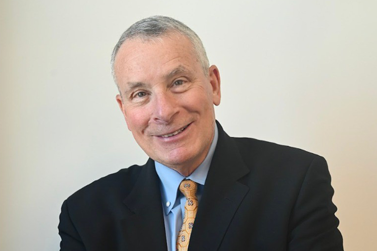 Smiling man in a dark suit and tie against a plain light background