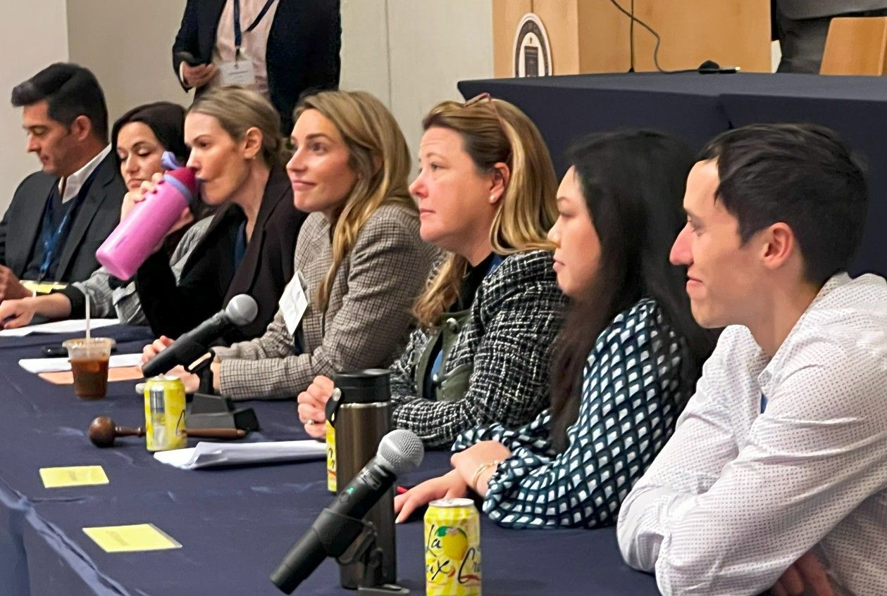 Panel discussion with six seated speakers at microphones on a conference stage