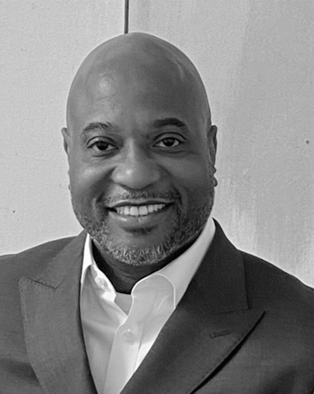 Smiling bald man in a suit and white shirt against a plain background