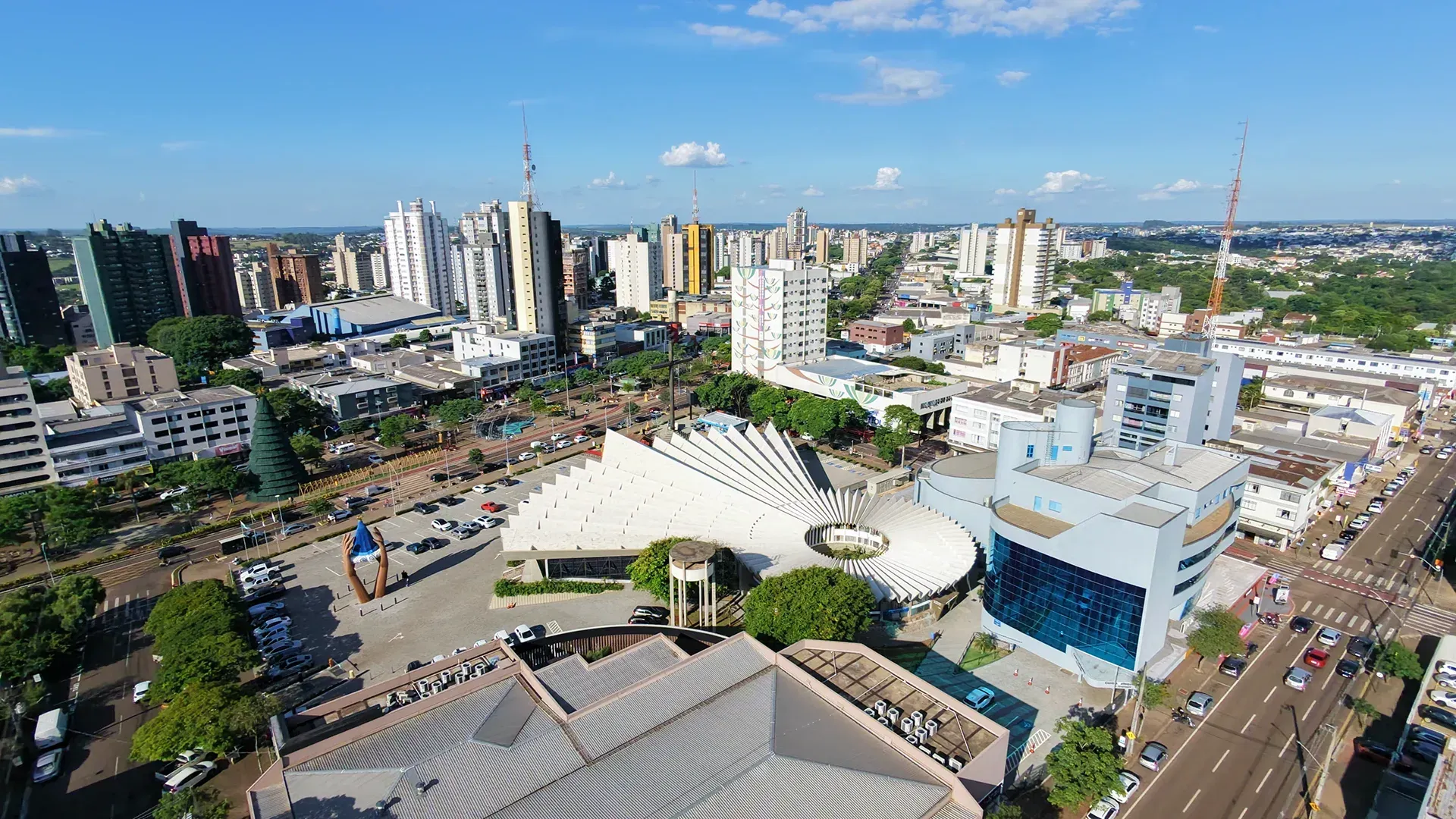 Vista aérea de uma cidade com prédios altos, uma grande estrutura branca e uma rua.