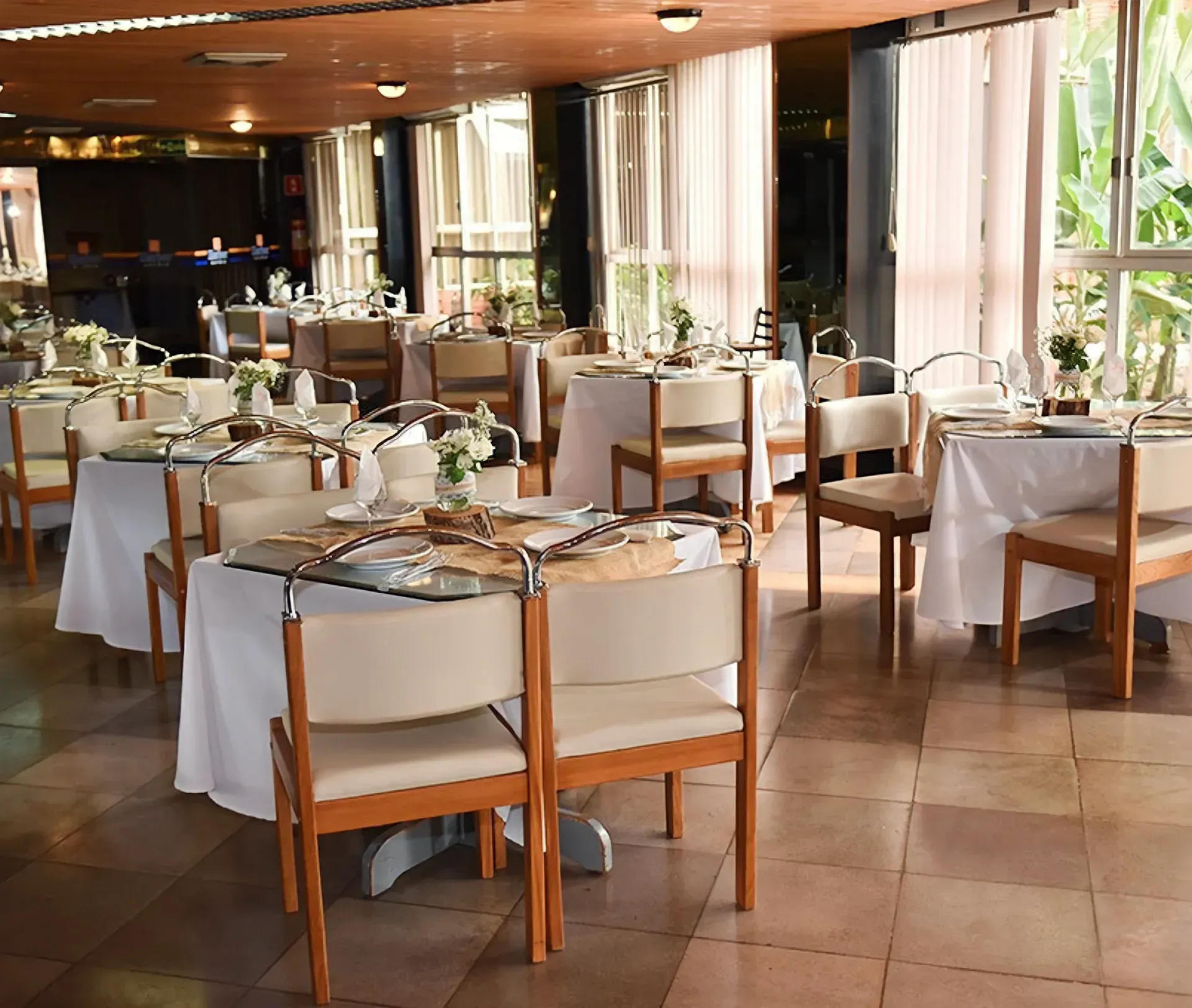 Sala de jantar de restaurante com mesas postas para os clientes, toalhas de mesa brancas e cadeiras.
