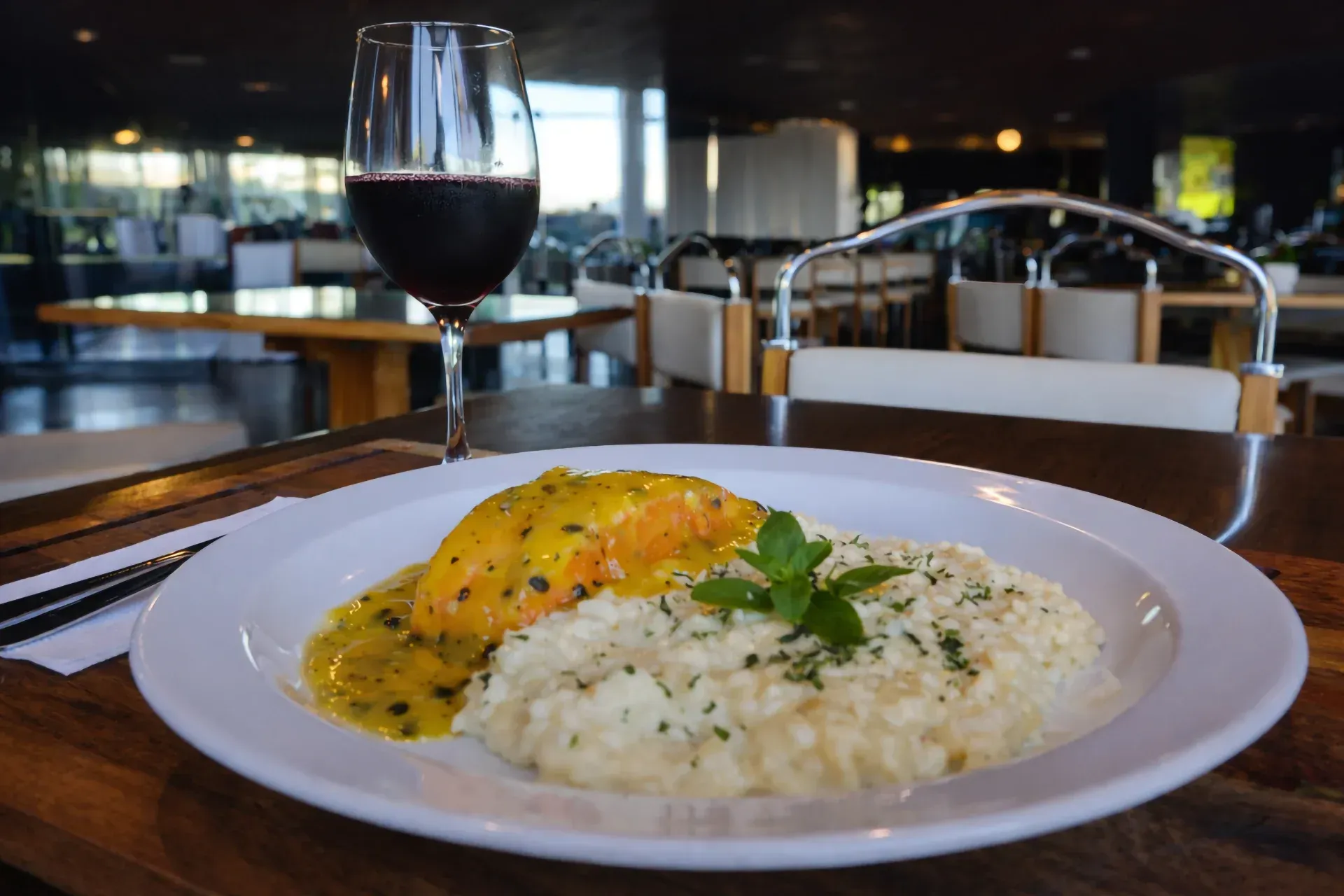 Prato de salmão com molho e risoto, taça de vinho, mesa de madeira, interior de restaurante.