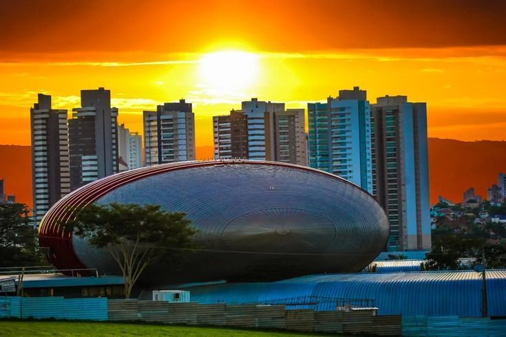 Pôr do sol sobre um grande e moderno estádio com prédios de apartamentos ao fundo.