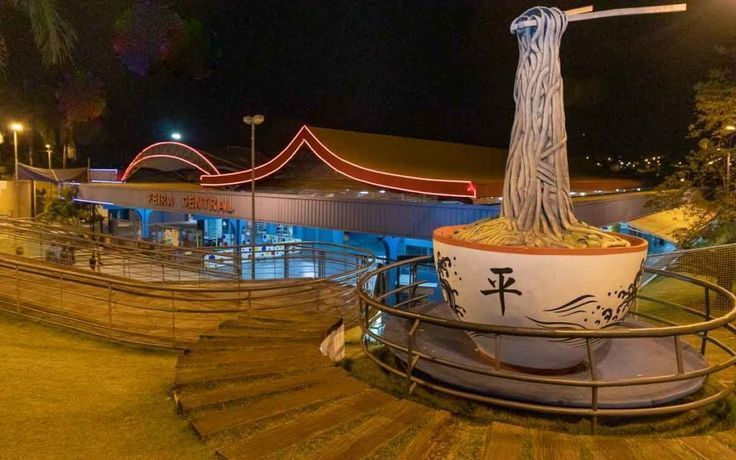 Vista noturna de um restaurante com uma escultura gigante de uma tigela de macarrão na frente.