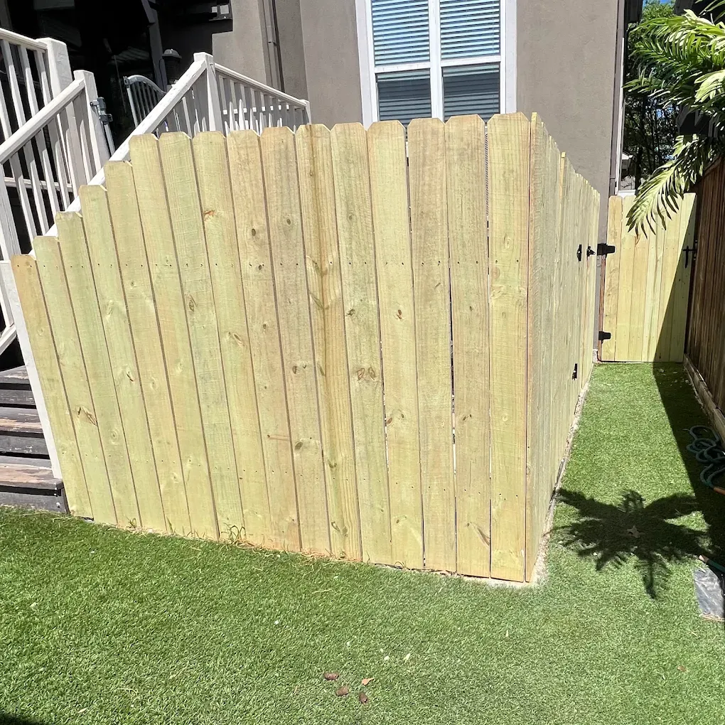 Yellow wooden fence panel beside a house, bordering a green lawn in bright sunlight