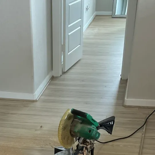 Green miter saw on a wood floor in a hallway with an open door and power cord nearby