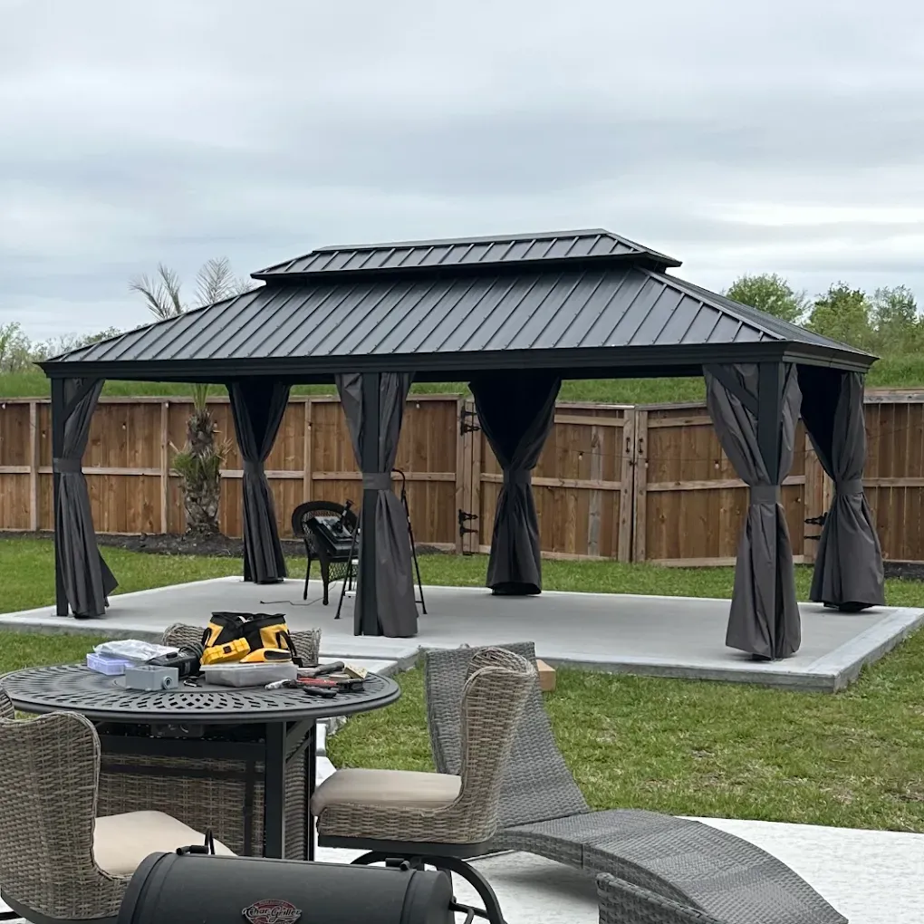 Black metal gazebo with gray curtains in a fenced backyard, with patio furniture in front