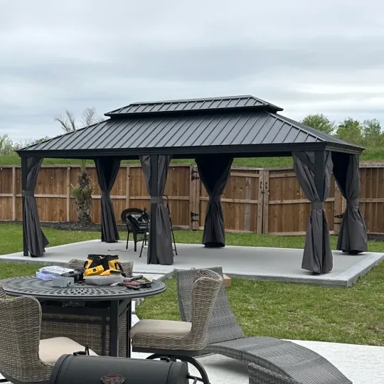 Outdoor black metal gazebo with curtains on a backyard patio, with a table and chairs in the foreground
