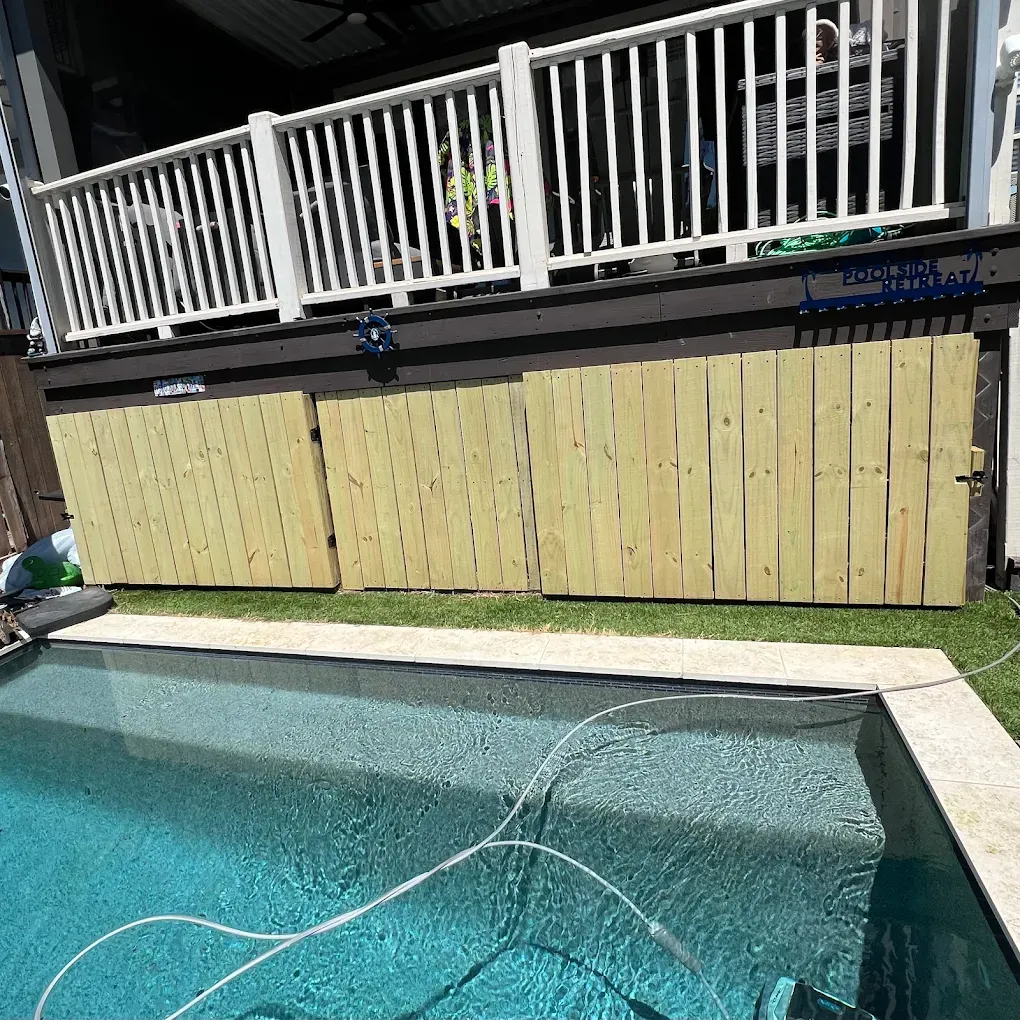Backyard pool with turquoise water, a white fence, and a wooden privacy barrier along the deck.