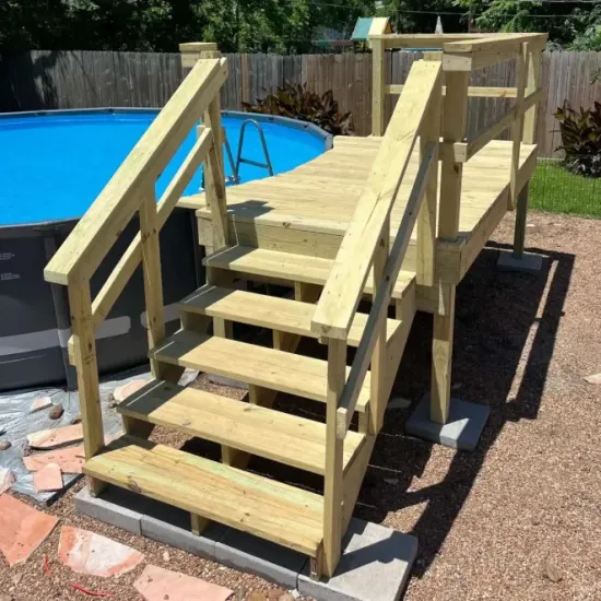 Wooden deck stairs and ramp beside a backyard pool, with handrails and support posts