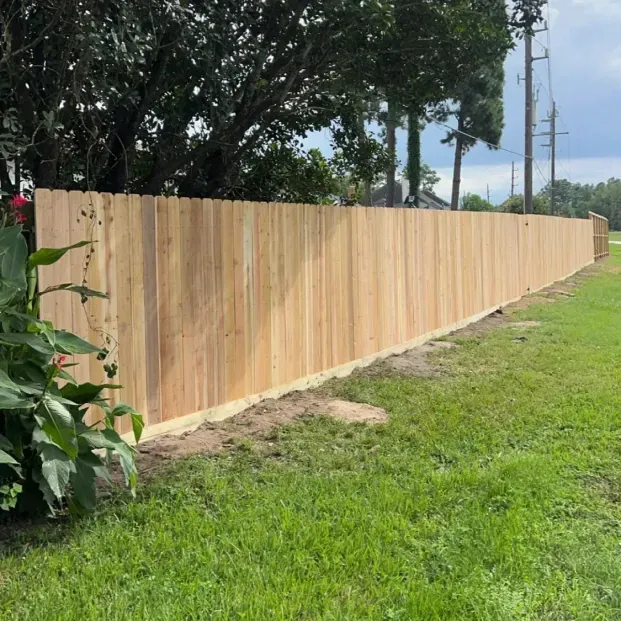 Freshly built wooden fence along a grassy roadside beside trees and utility poles.